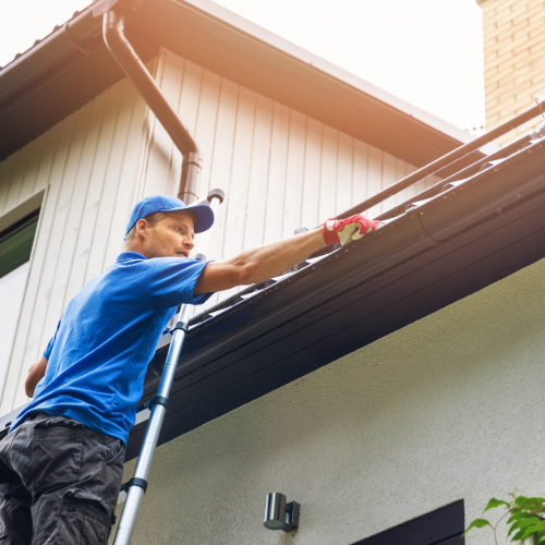 Professional technician on a ladder performing gutter system repairs and maintenance on a residential home.