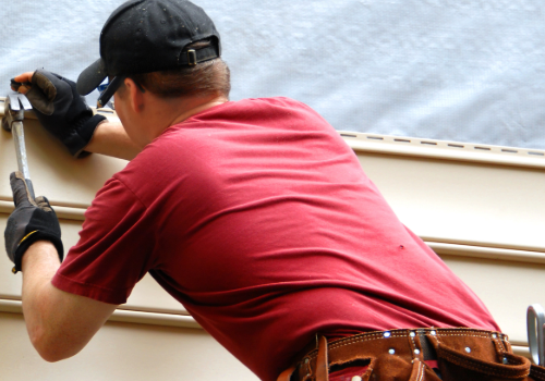 Professional installer in a red shirt and cap working on exterior home siding.