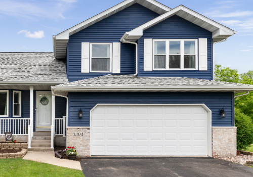 Newly repaired residential roof on a modern two-story home with a white garage door and lush front yard