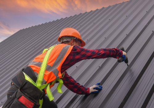 Professional roofer installing a metal roof on a commercial building at sunset, wearing safety gear.